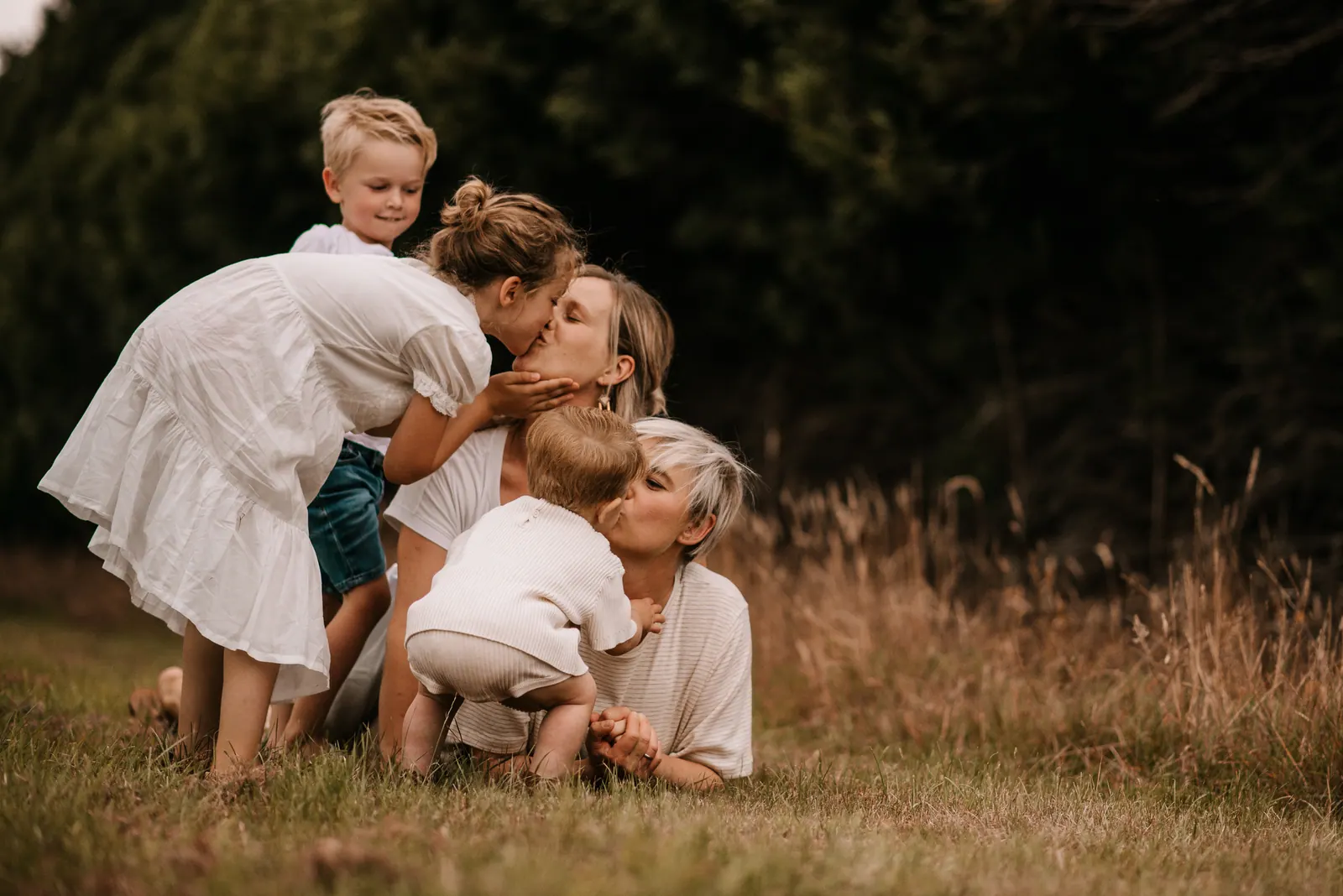 Moeder, grootmoeder en twee kleine kinderen knuffelen elkaar in het hoge gras tijdens een familiefotoshoot